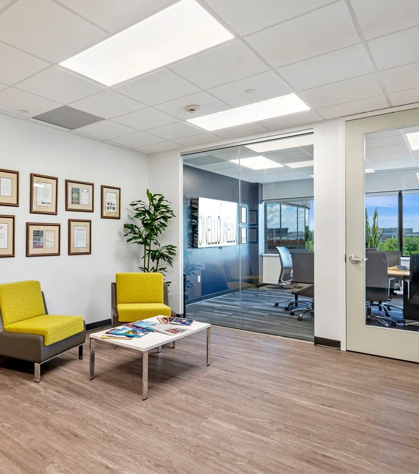 An office lobby with yellow chairs looking through glass windows into a conference room